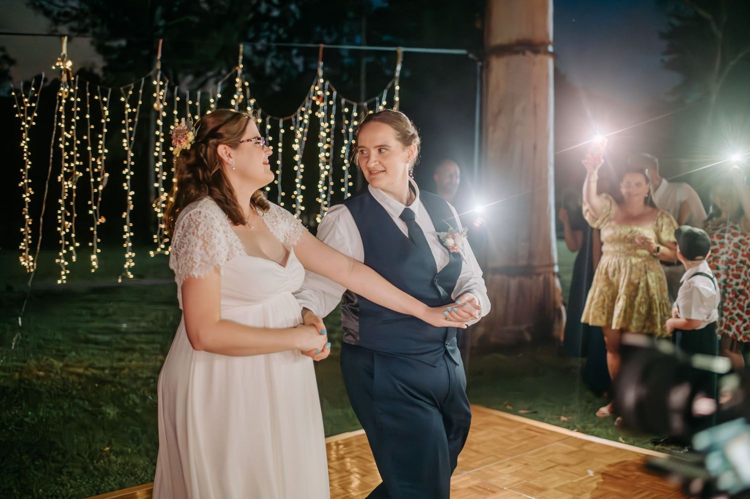 Couple dancing together under twinkling string lights at nighttime wedding reception.