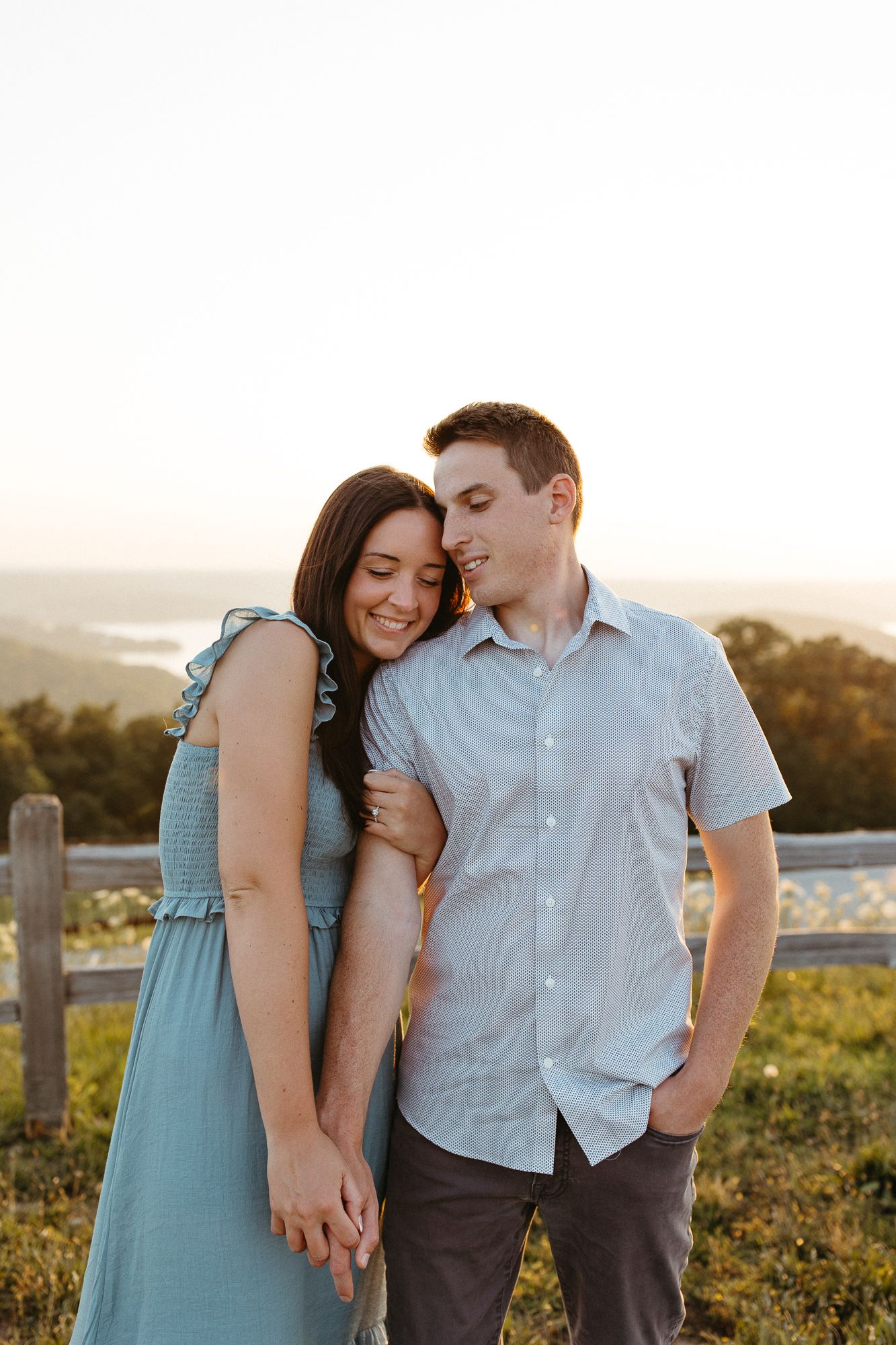Romantic couple embracing during sunset photo session in countryside setting.