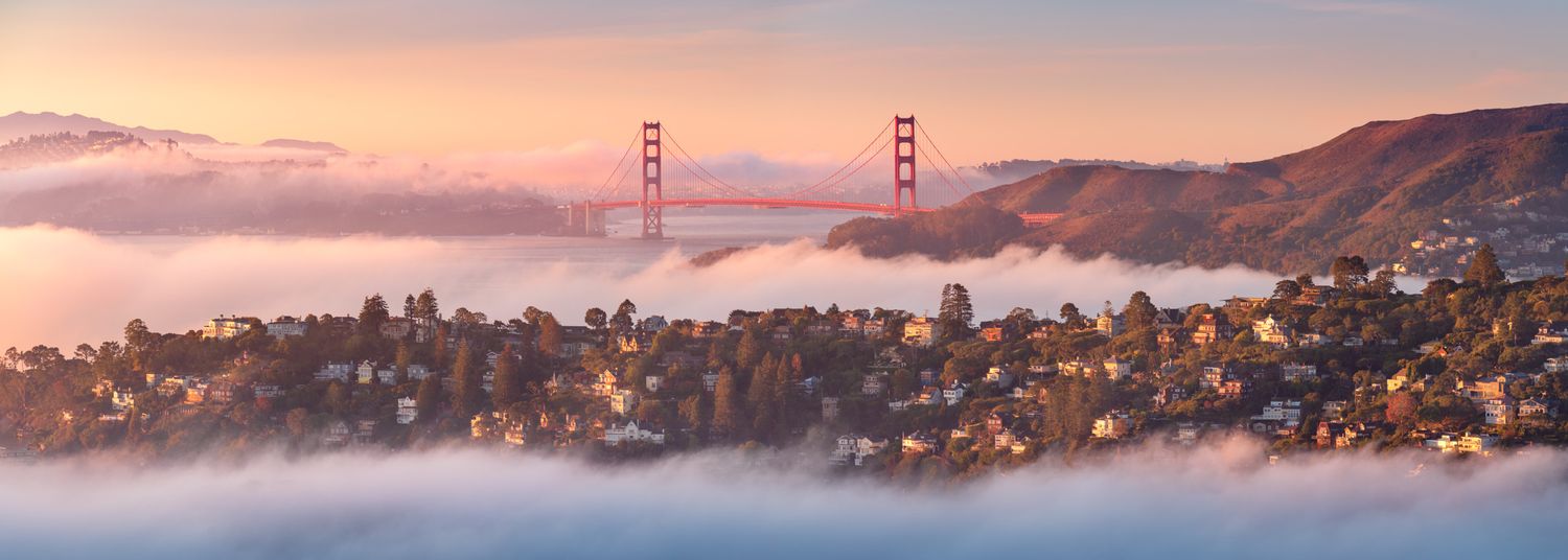 San Francisco's Golden Gate Bridge towers emerge through low-lying fog at sunrise.