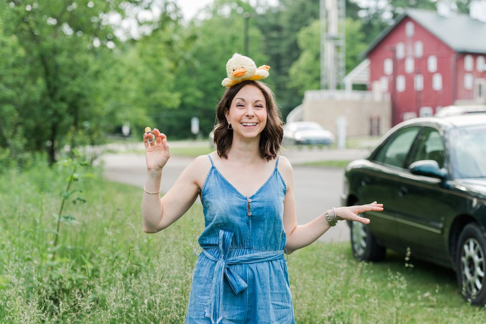 Woman in blue denim dress enjoying a sunny day outdoors near a red barn.