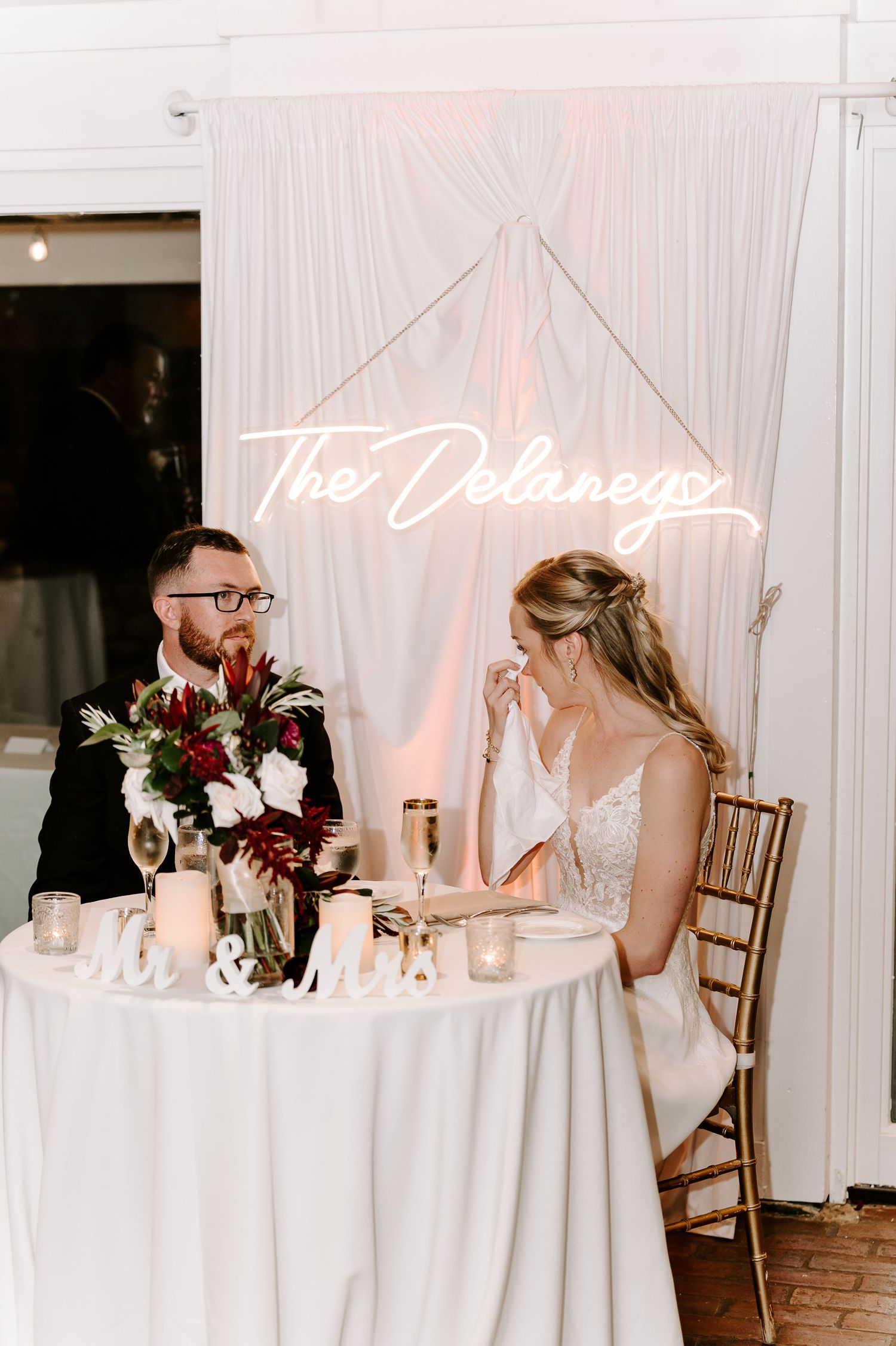 Intimate wedding reception scene with candlelit table and white drapery backdrop.