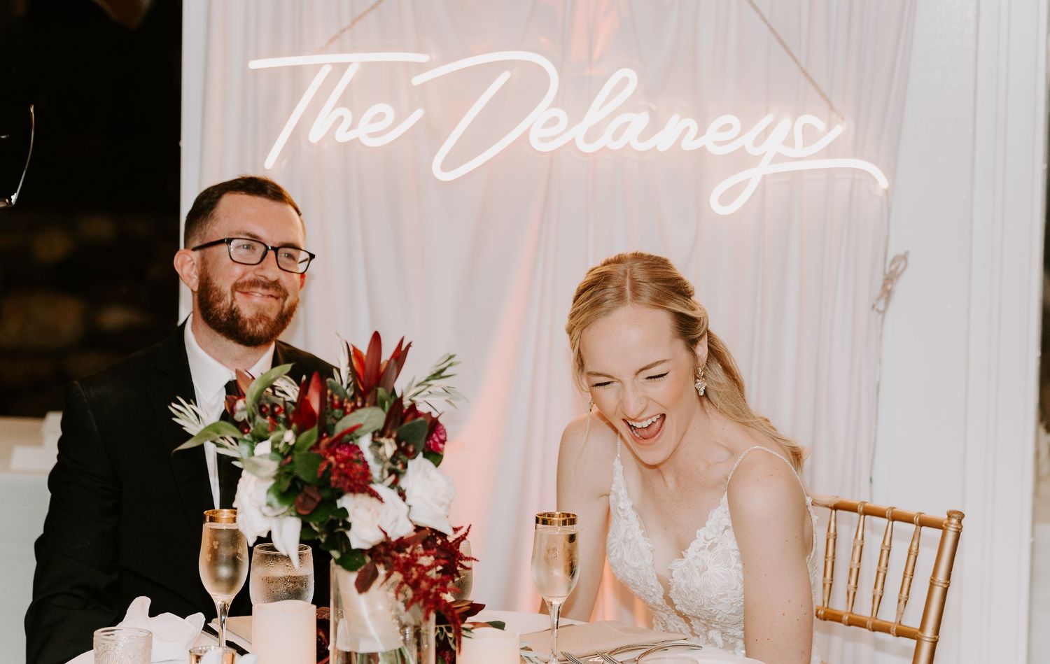 Elegant wedding reception table with white linens and neon signage in the background.