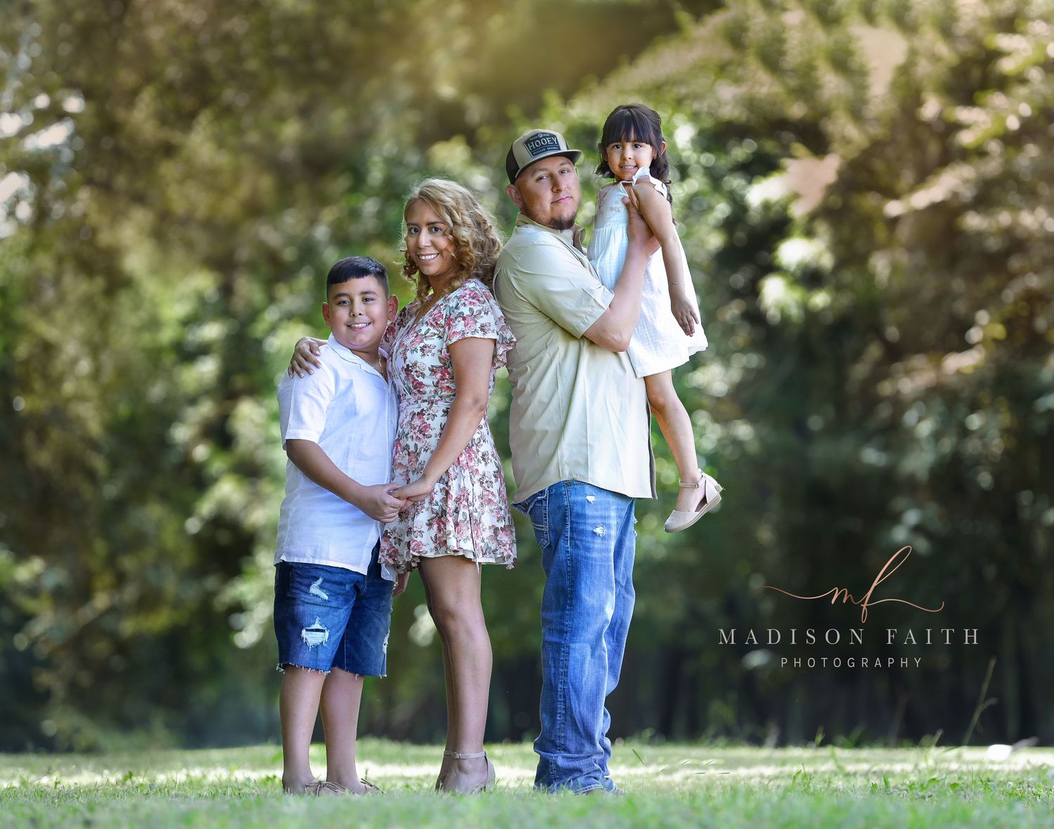 A family enjoys a casual outdoor photoshoot in a sunlit garden setting.