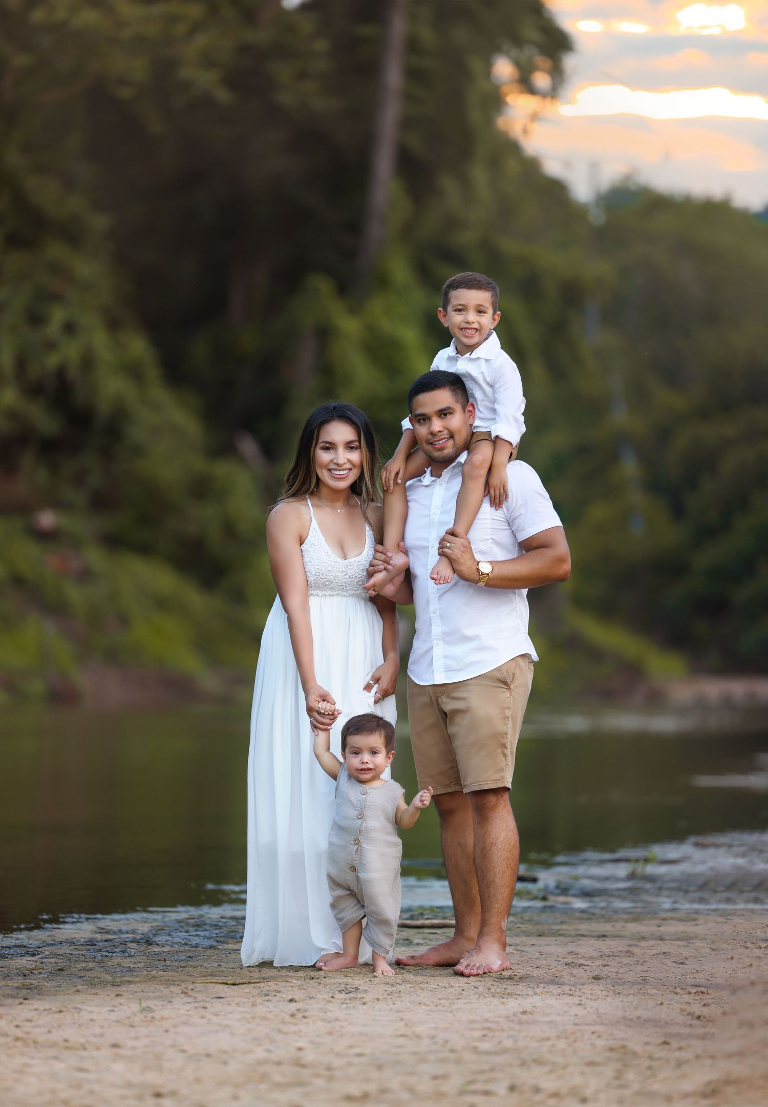 Family portrait at sunset by riverside in white and neutral clothing.