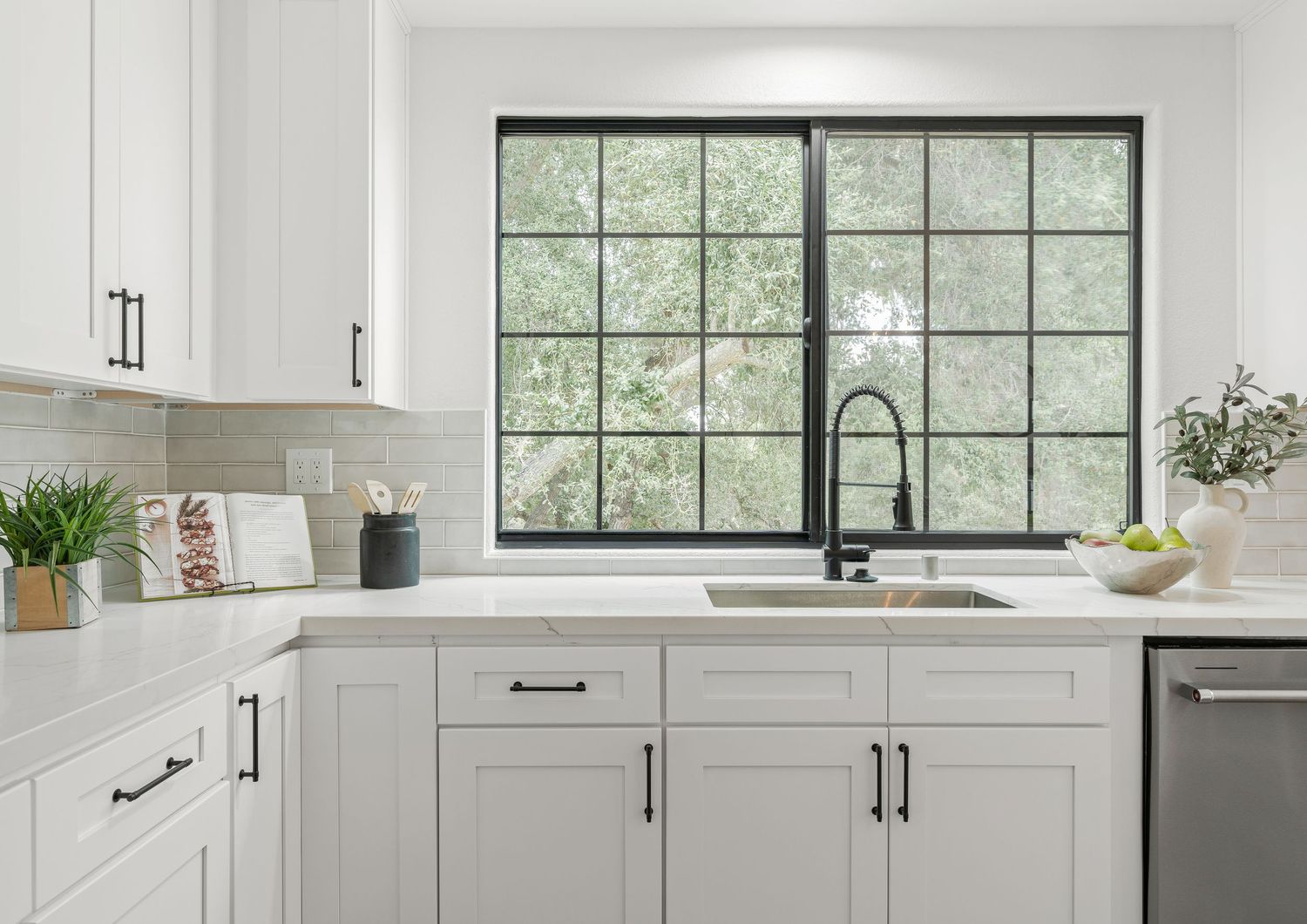 Modern white kitchen with black-framed windows and shaker cabinets in bright natural light.