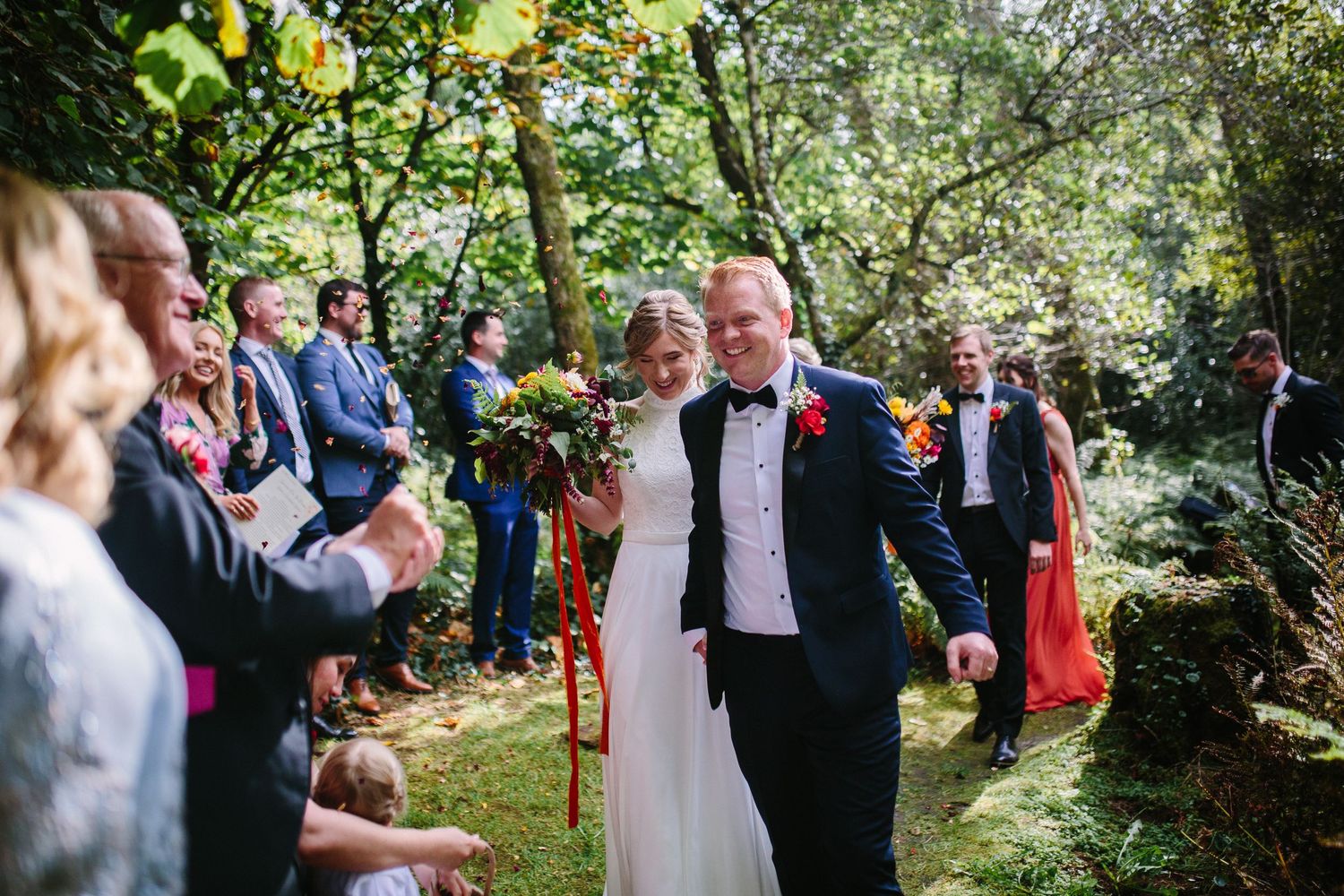 Wedding couple walking through guests throwing confetti in a lush garden setting.
