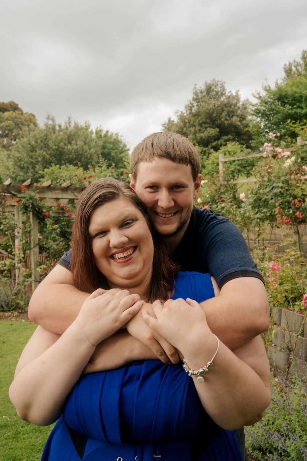 Plus size couple dressed in dark blue embracing in park on cloudy day