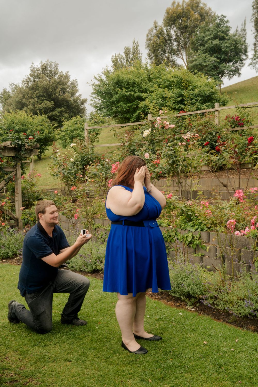 man on one knee holding engagement ring to surprise plus size girl dressed in blue