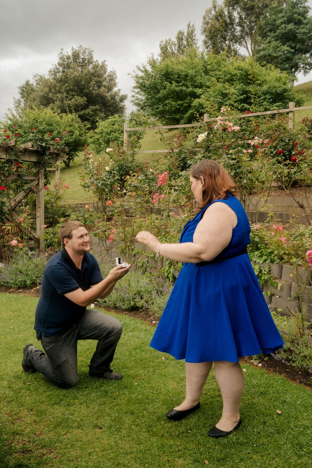 plus size girl in blue dress surprised by boyfriend proposing on one knee
