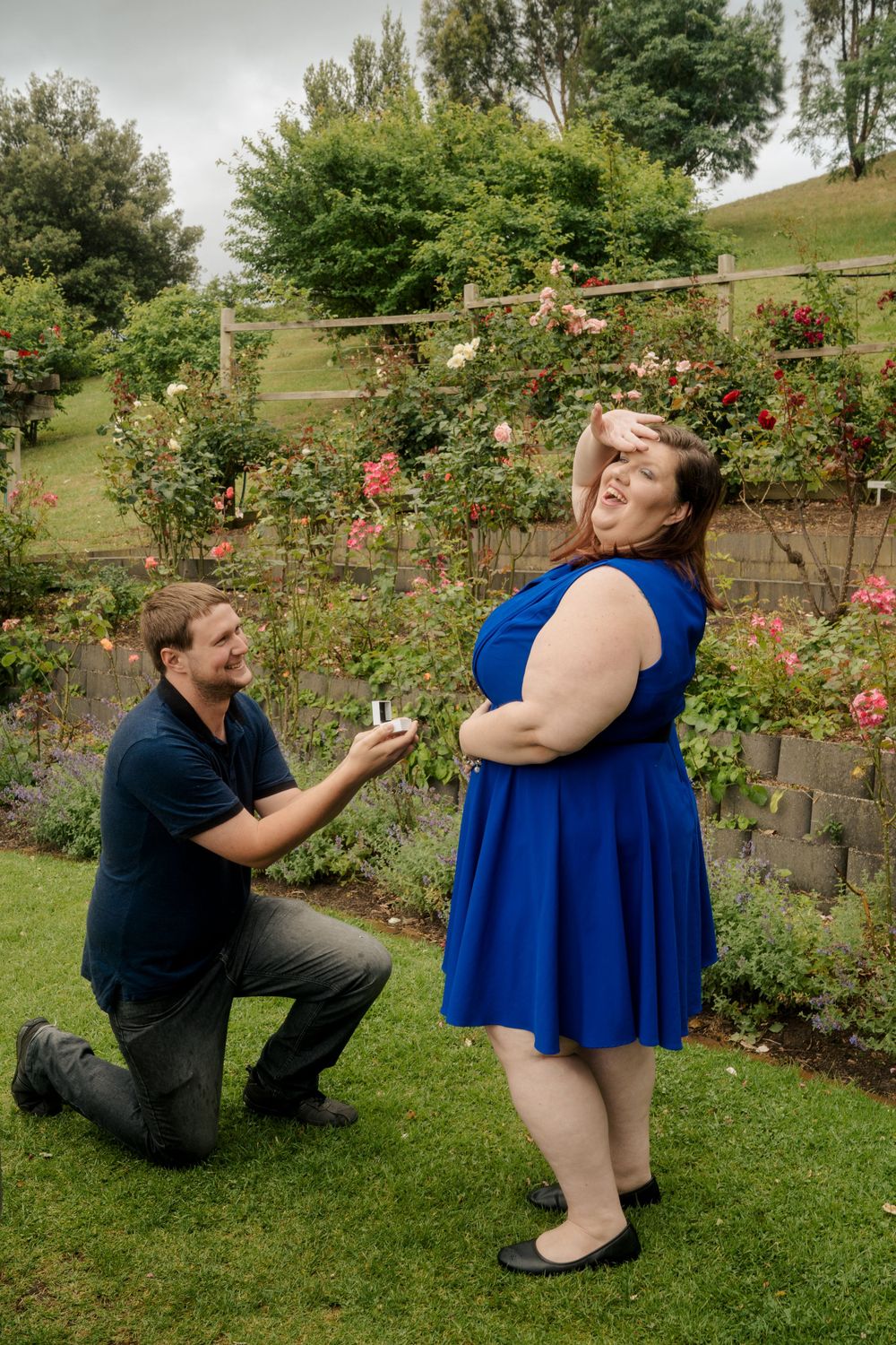 plus size couple hamming up proposal with engagement ring in park