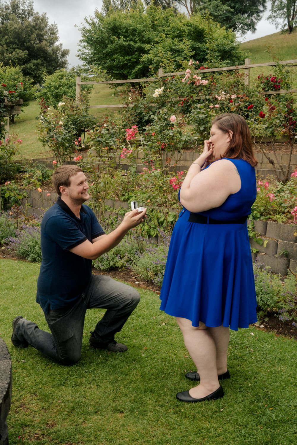 plus size girl in blue dress being surprised with proposal and engagement ring by boyfriend.
