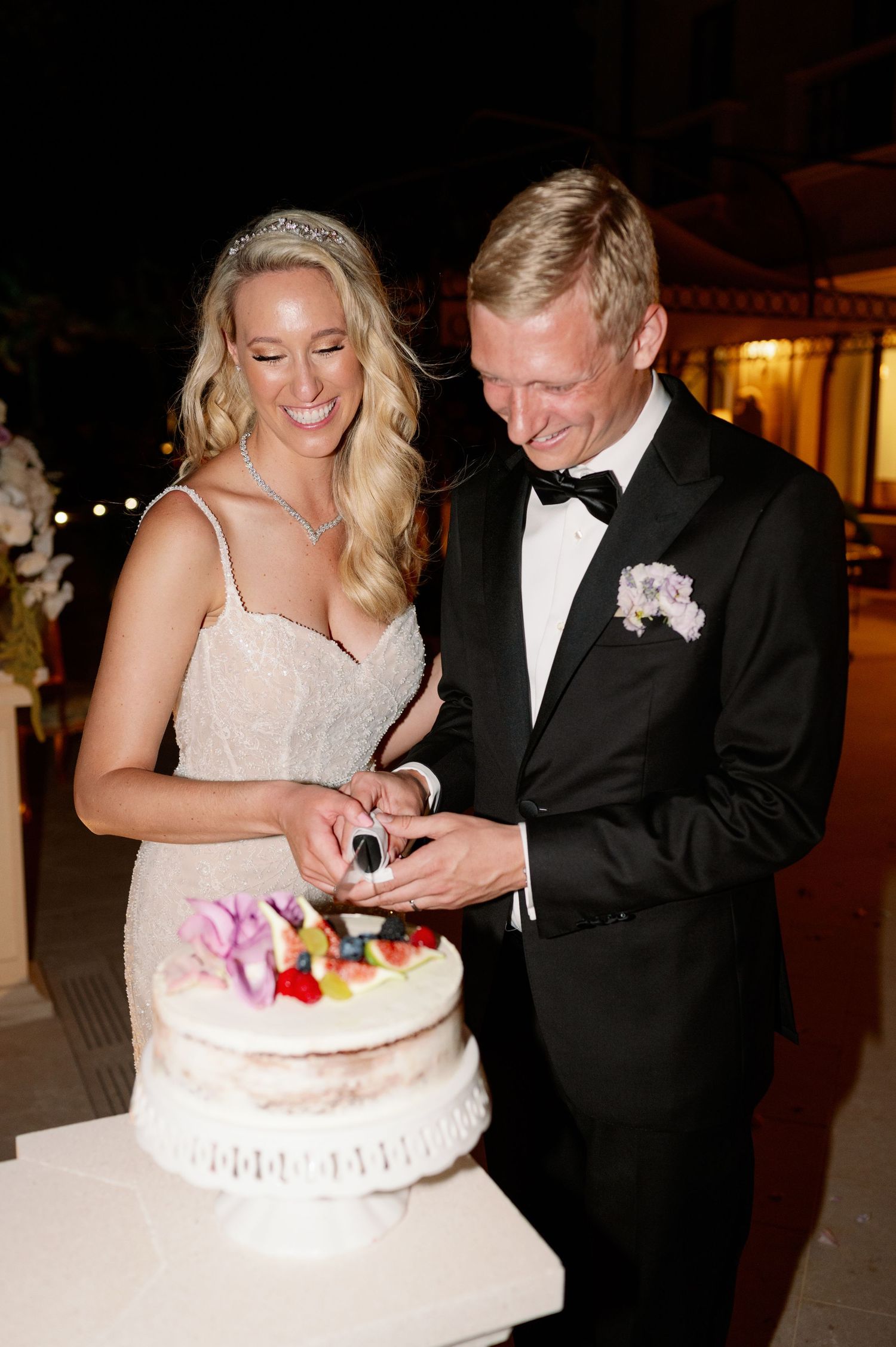 Newlyweds cutting their white wedding cake decorated with fresh fruits.