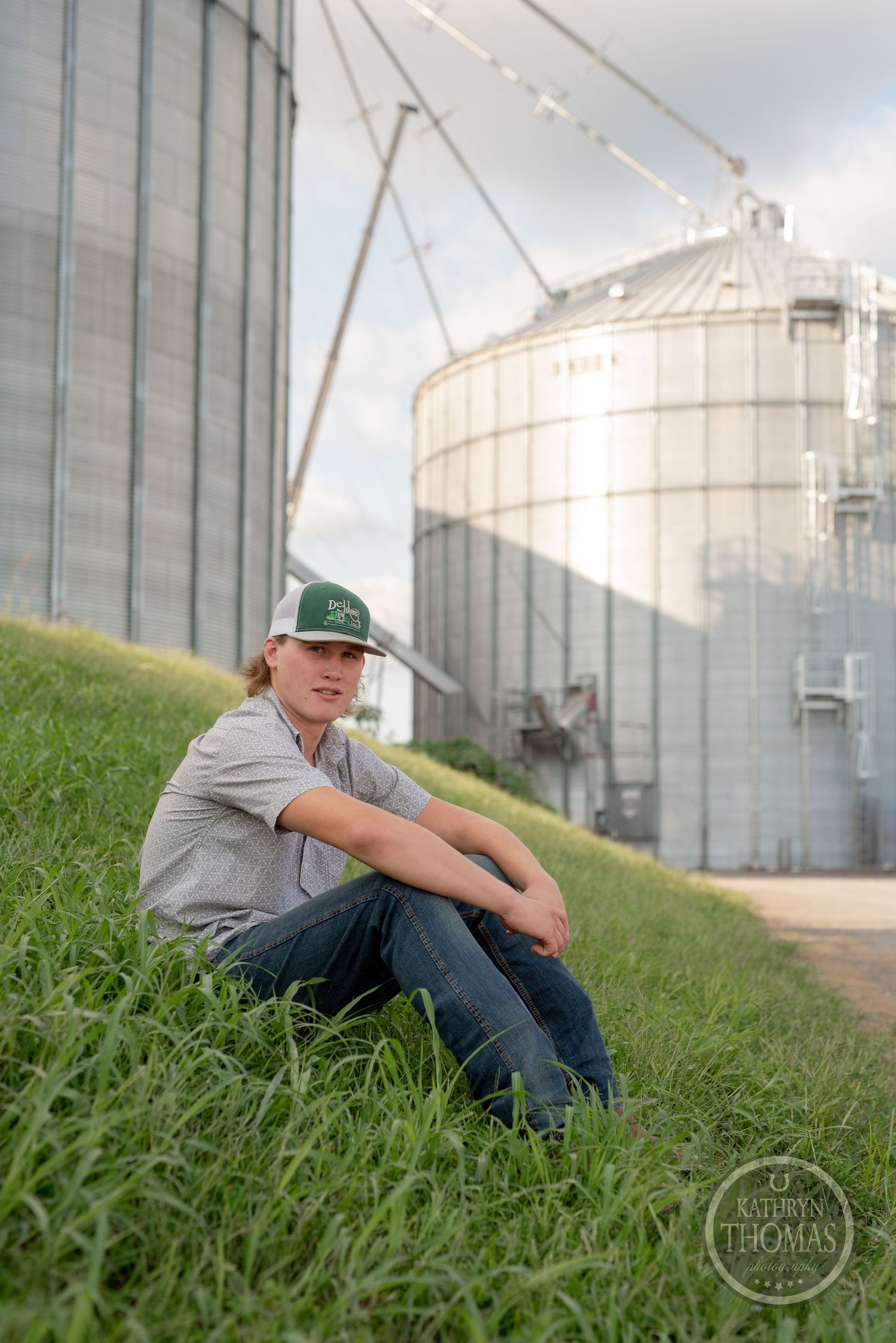 Peaceful rural scene with someone resting on grassy hill beside metal grain storage silos.