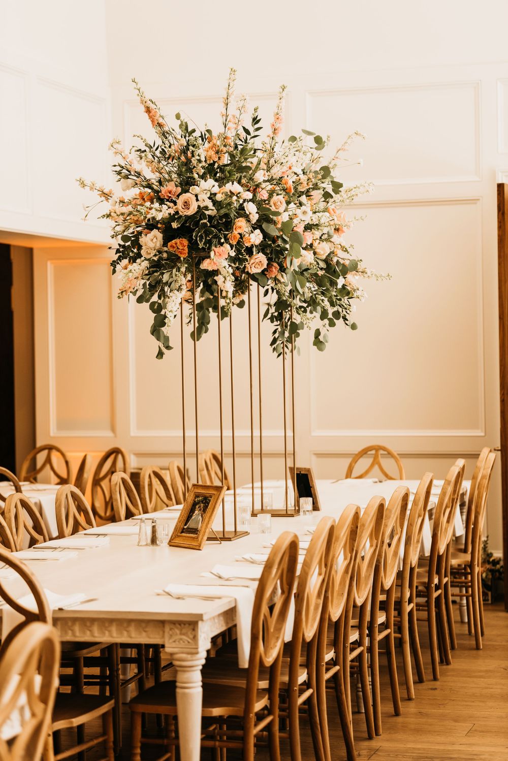 White and peach floral centerpiece arrangement on gold stand with elegant table settings.