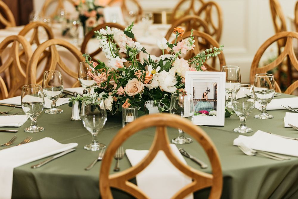 An elegant table setting with sage green linens, wooden chairs, and white floral centerpieces.