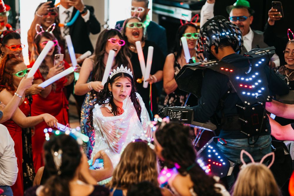 Guests surround dancer wearing light-up accessories during energetic wedding reception celebration.