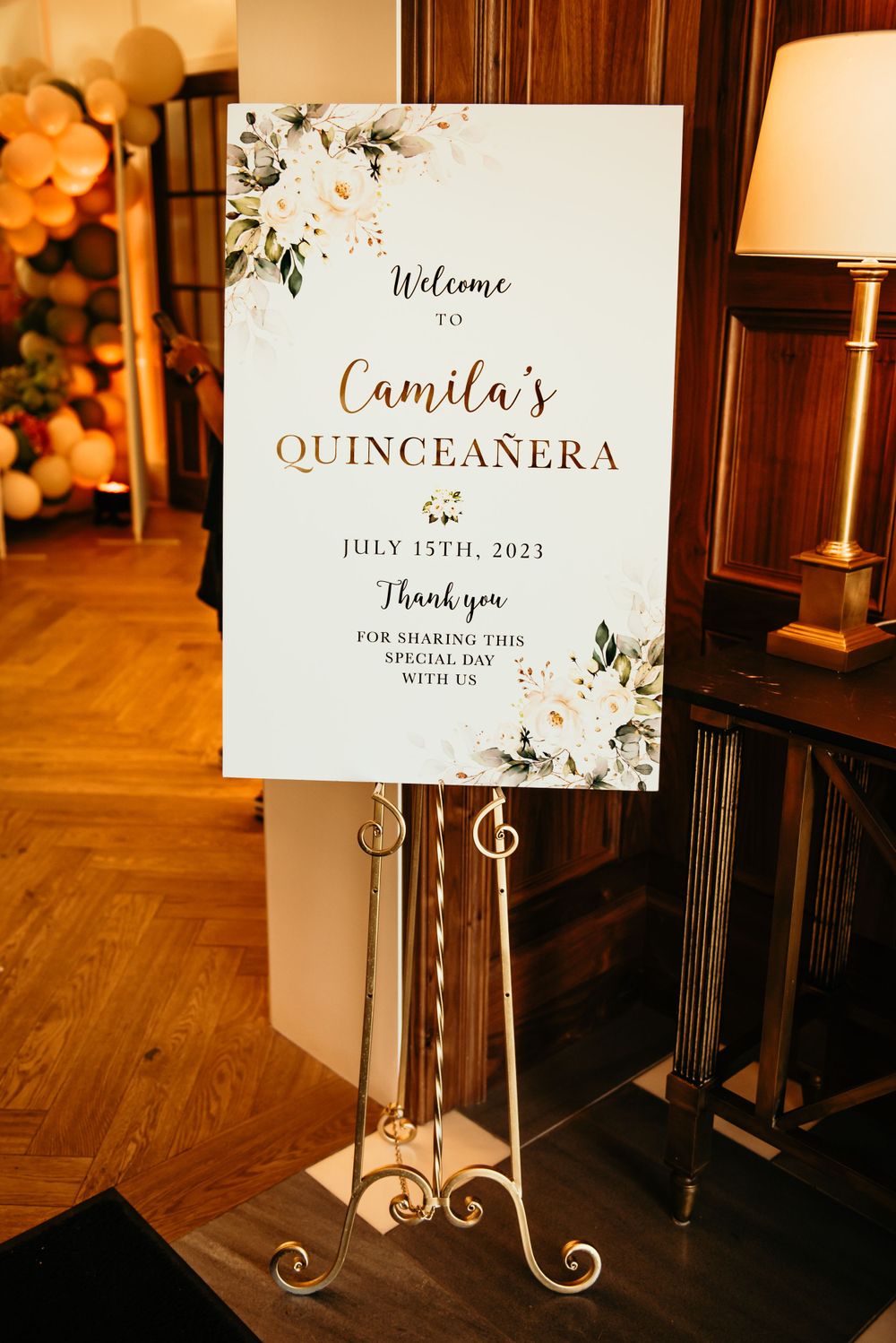 An elegant welcome sign for a quinceañera celebration featuring floral designs and gold lettering.