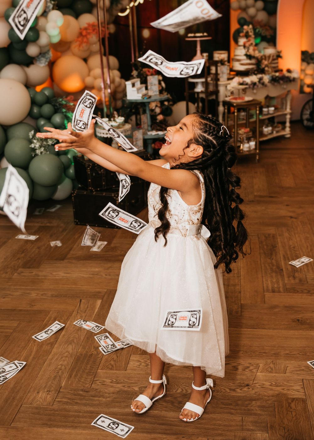 White-clad celebrant joyfully throwing money in the air surrounded by balloon decorations.