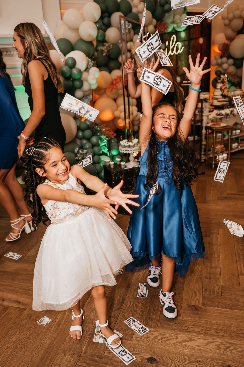 Young attendees in formal dresses playing with falling money at a celebration.