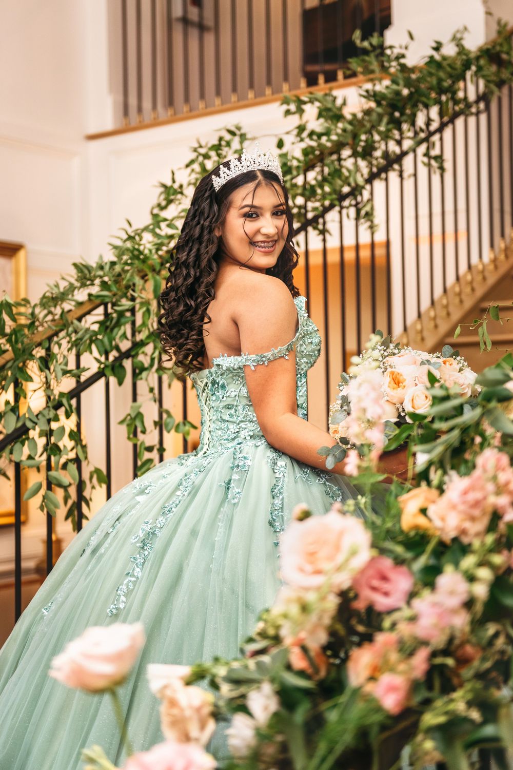 A mint green ball gown with floral decorations photographed on a staircase with pink roses.