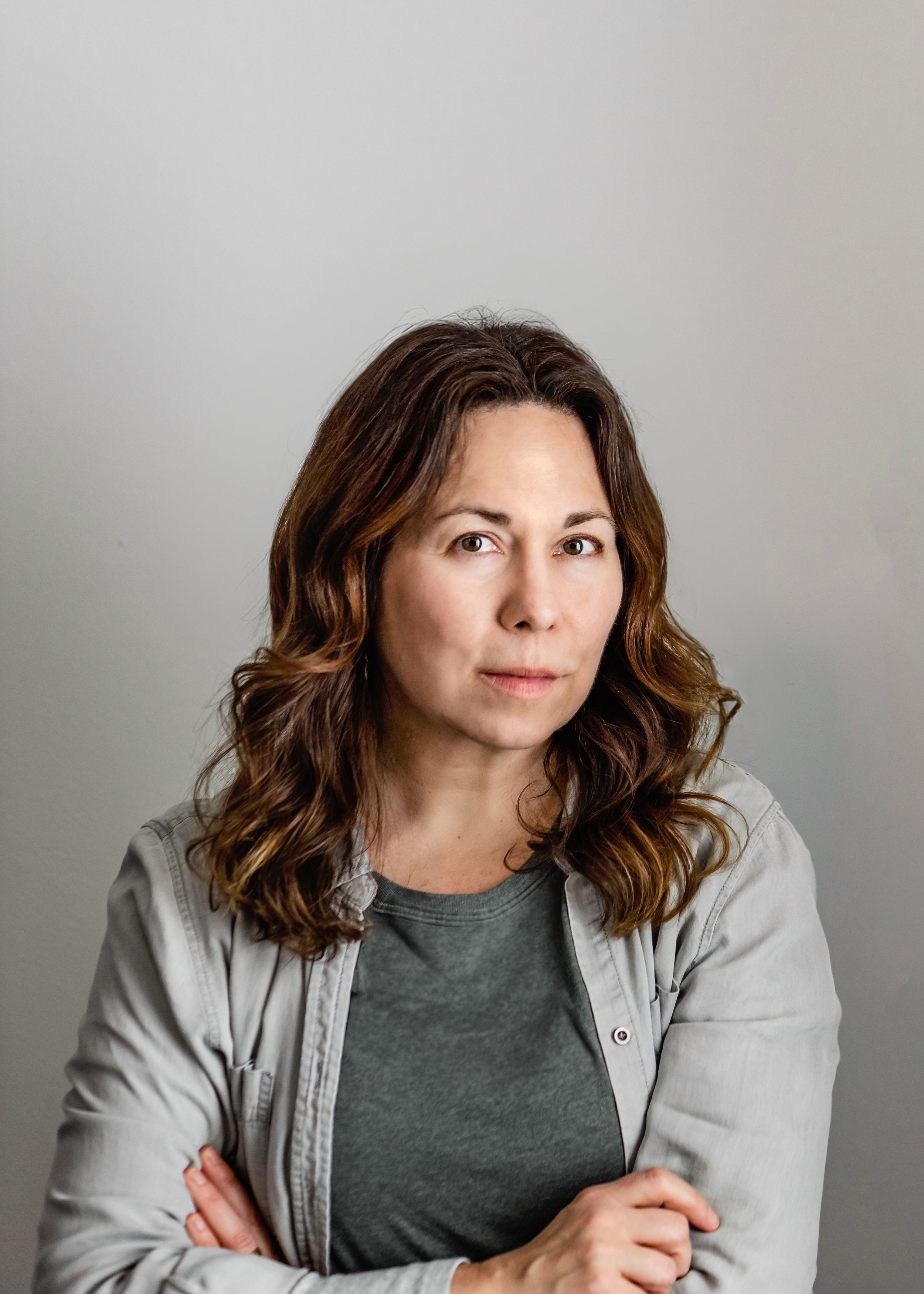Professional headshot against gray background wearing casual gray jacket.