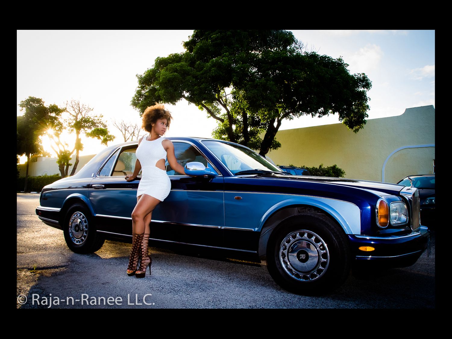 Outdoor photoshoot with a classic blue luxury car against a sunset backdrop.