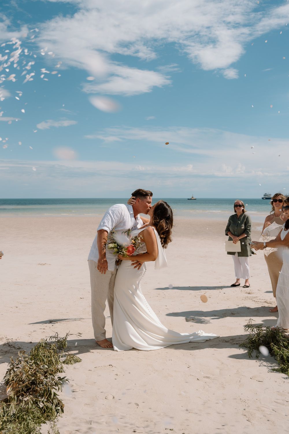 Wedding party lined up on a sunny beach taking photos together.