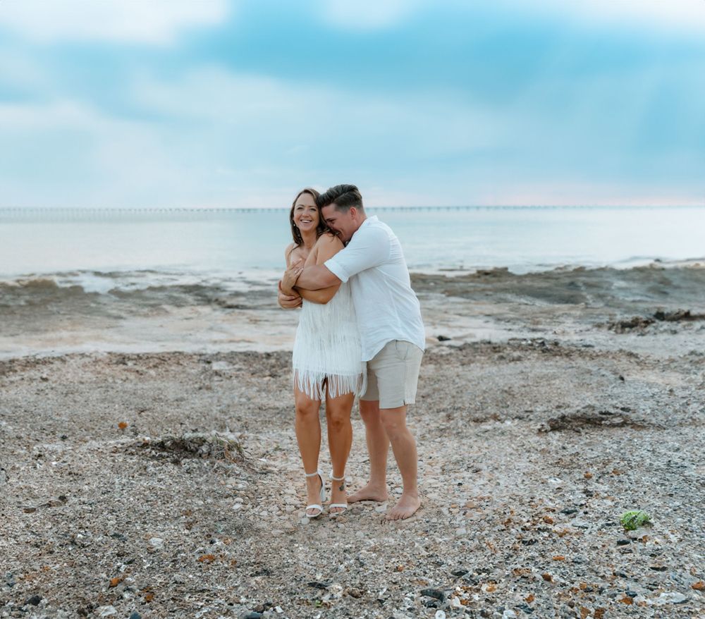 Couple walking along a rocky beach shoreline at sunset.