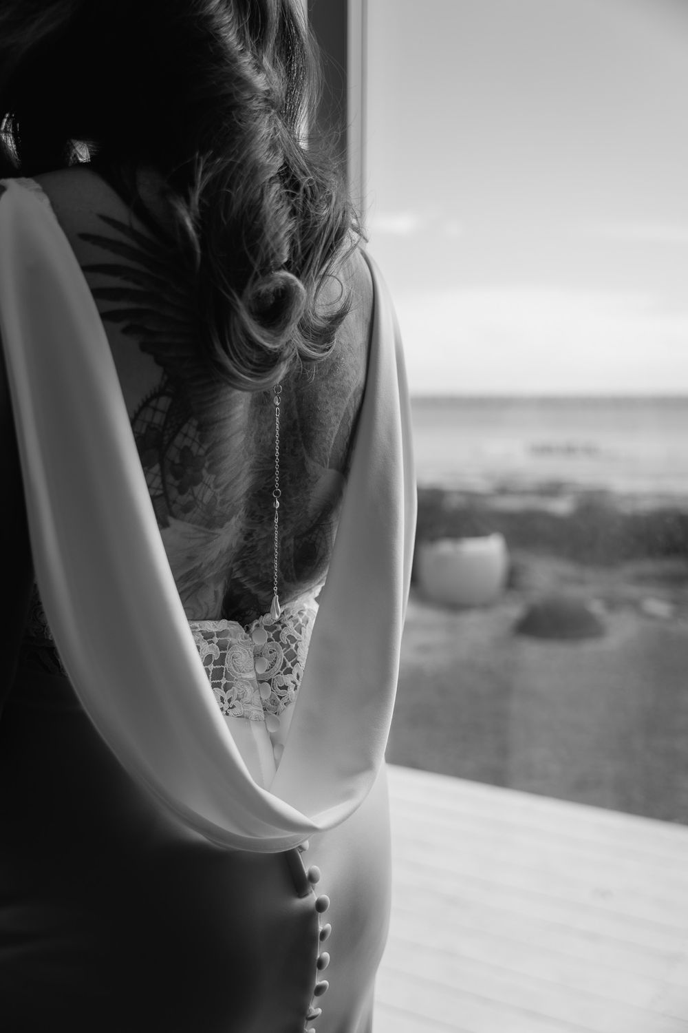 Back detail of a wedding dress with buttons against a window overlooking a landscape.