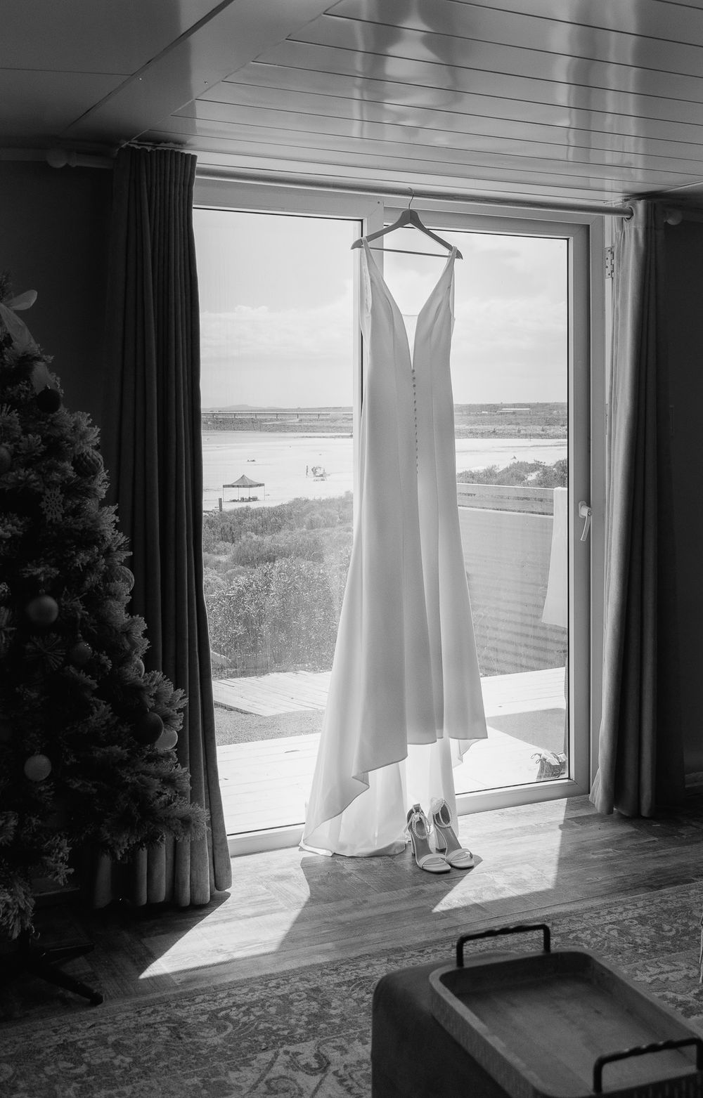 Wedding dress hanging in window frame with ocean view in background.