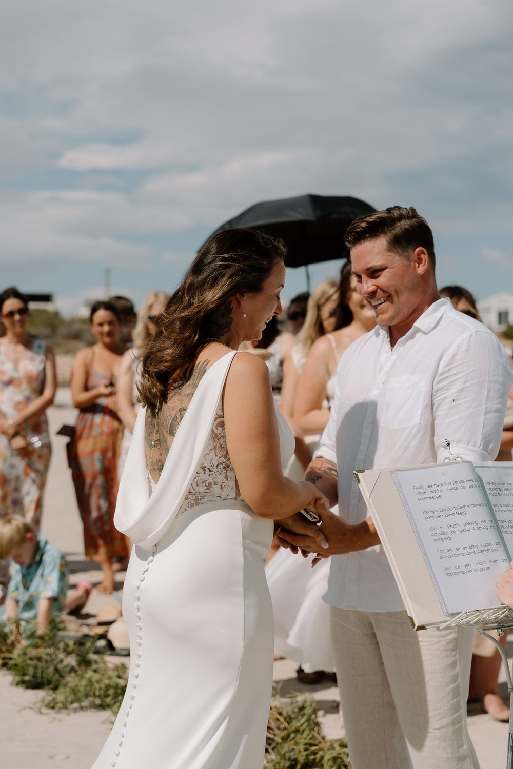 Beach wedding ceremony with attendees dressed in white and khaki reading from ceremony programs.