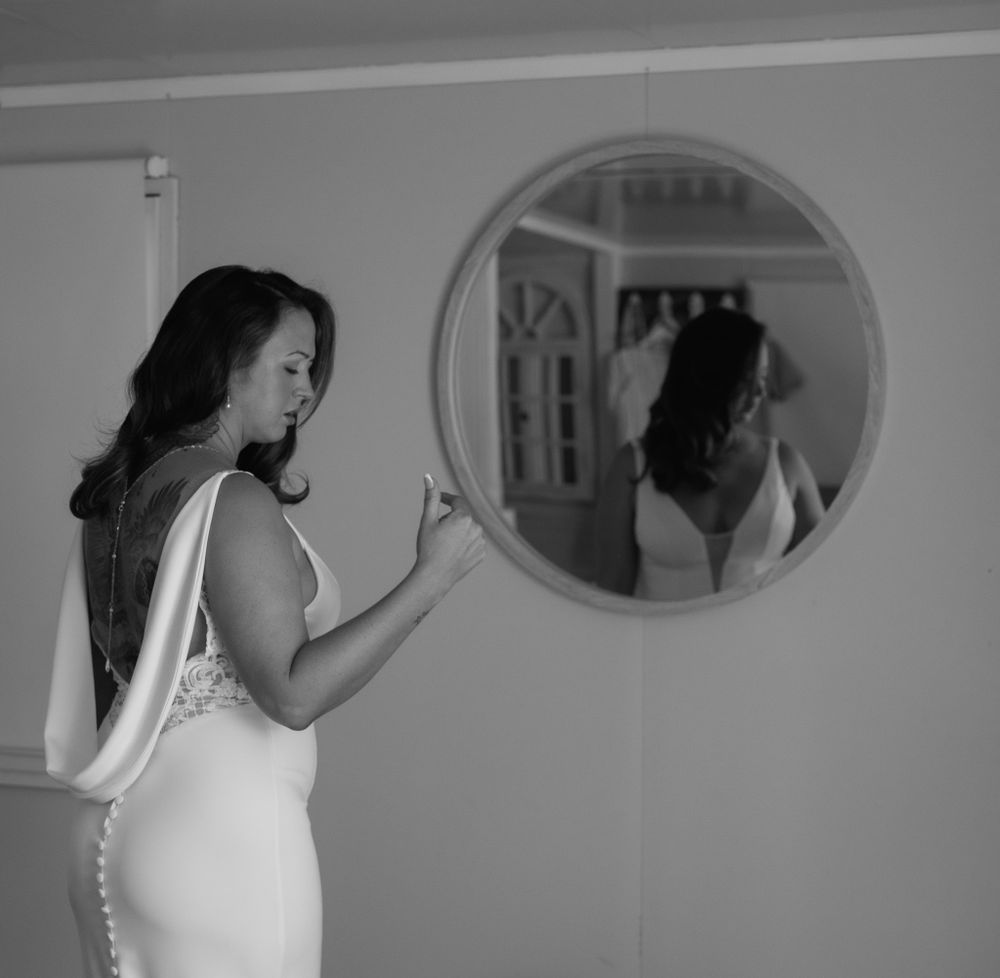 Black and white photo of someone in a wedding dress looking in a round mirror.