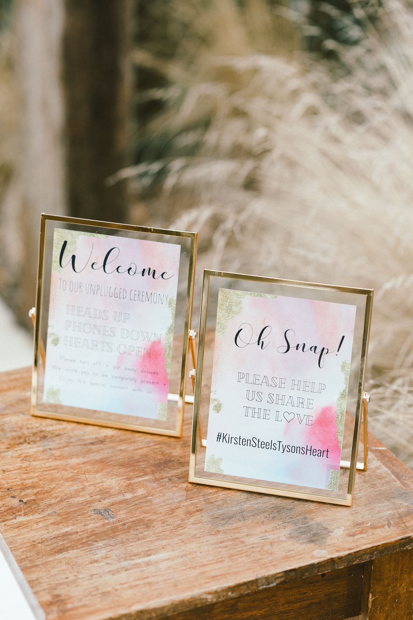 Gold-framed welcome signs with watercolor details on wooden table.
