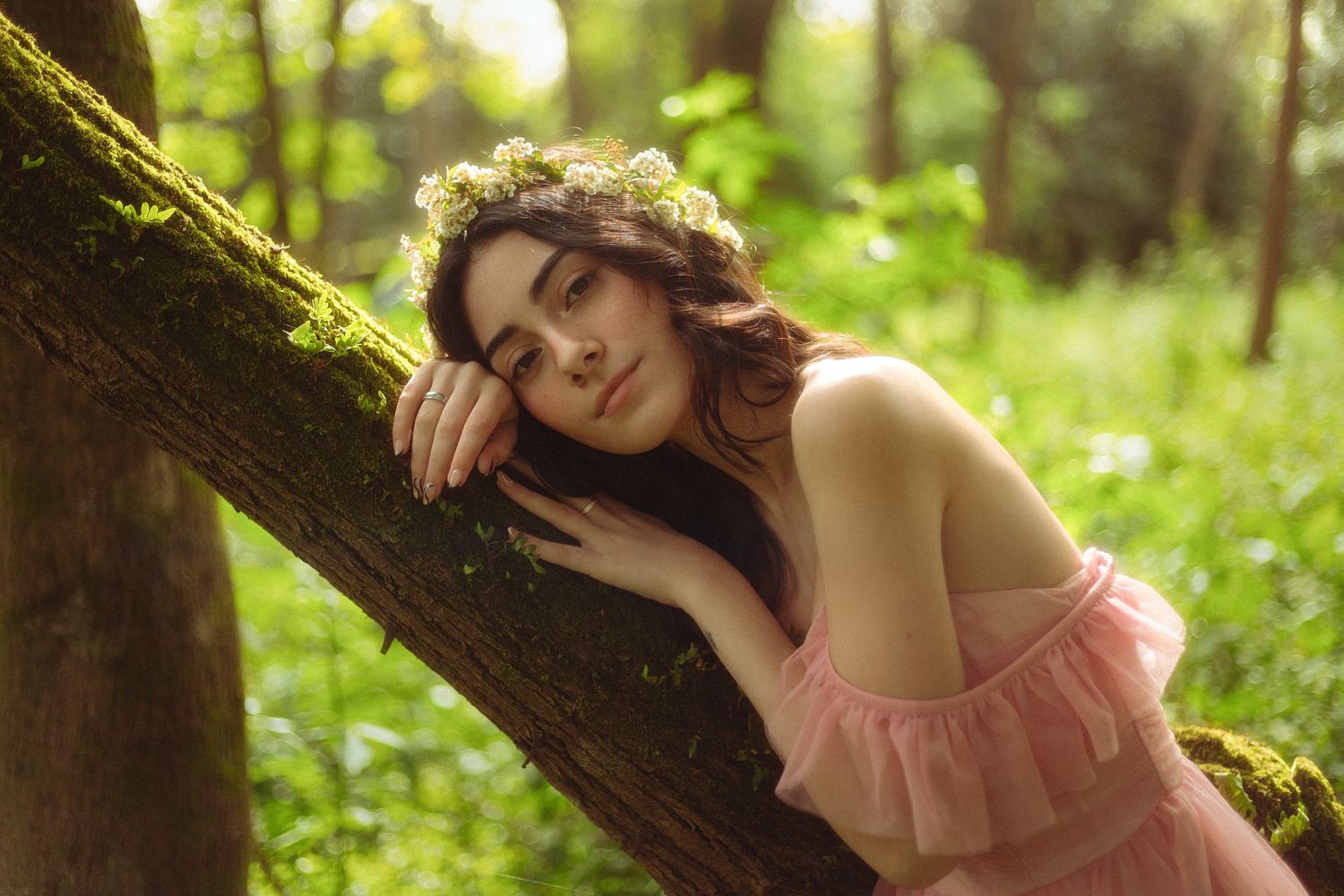 mulher fada ninfa de vestido rosa e coroa de flores em floresta encostada deitada árvore fantasia fairycore