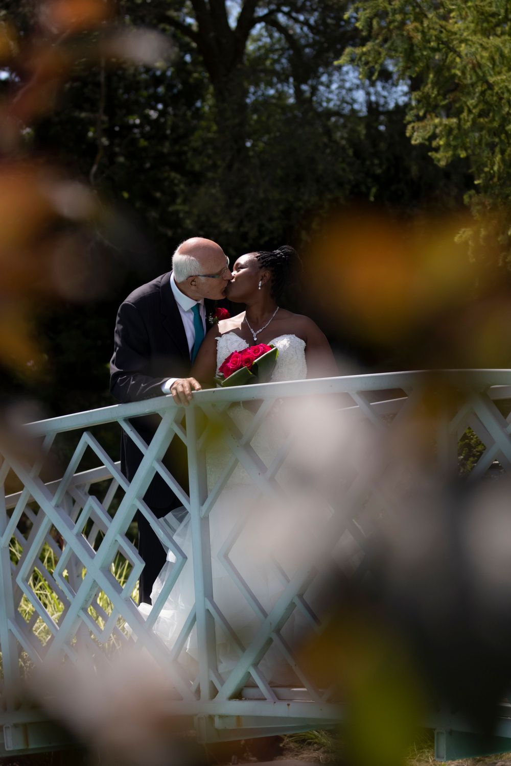 Focus on bride and groom on a bridge kissing framed with blurred trees