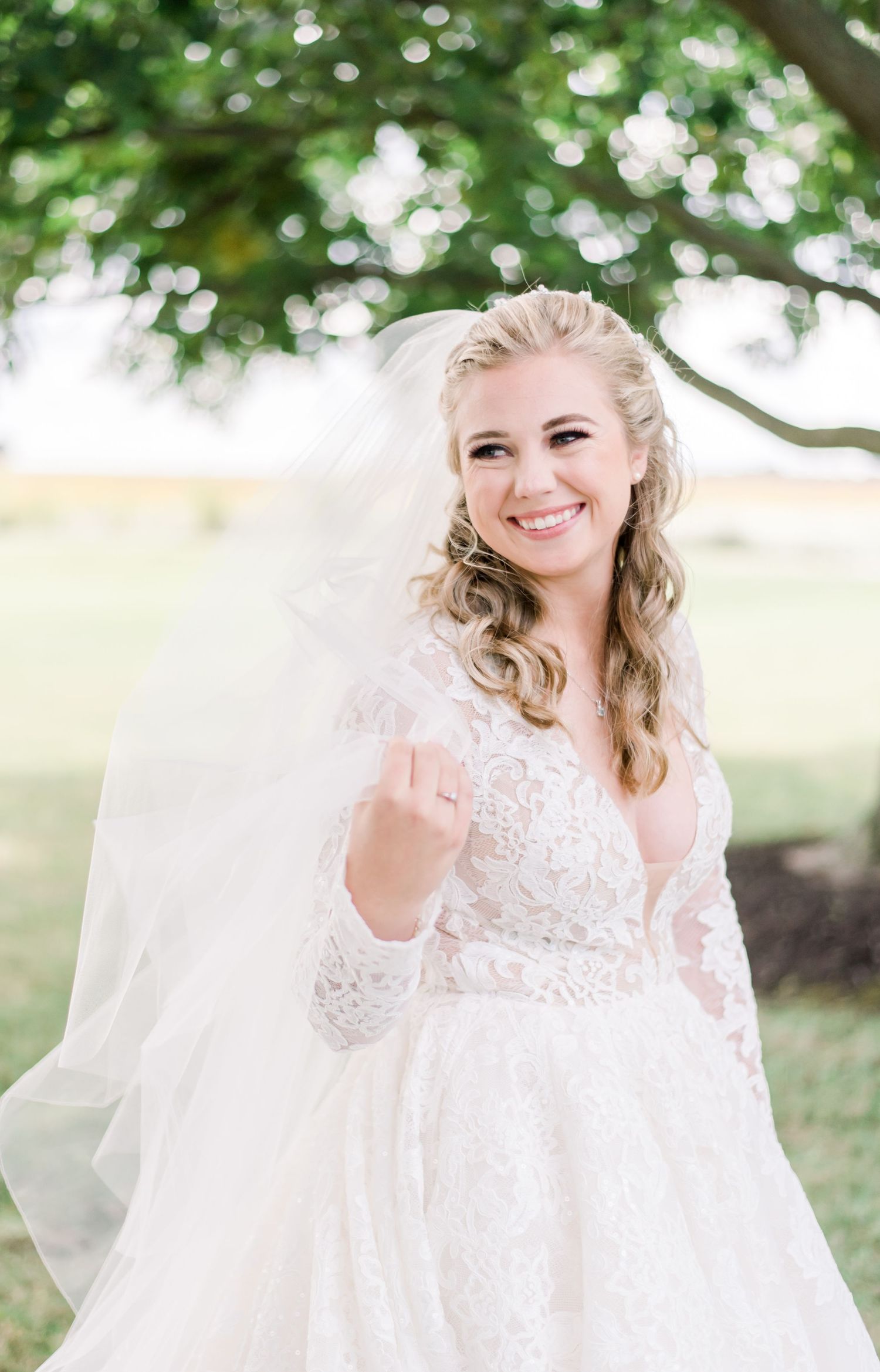 Joyful bride in lace wedding dress and veil outdoors under tree canopy. Indianapolis, Indiana. Angela Hartwig Photography.