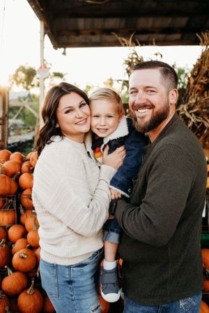 Autumn family portrait at a pumpkin patch with orange pumpkins in the background.