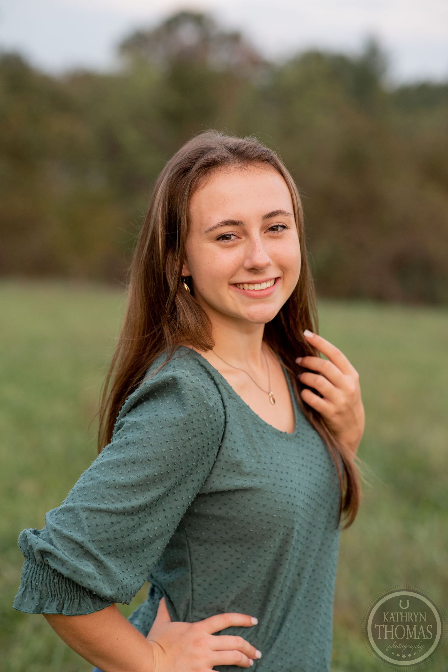 Cheerful outdoor portrait with natural lighting and a green countryside backdrop.