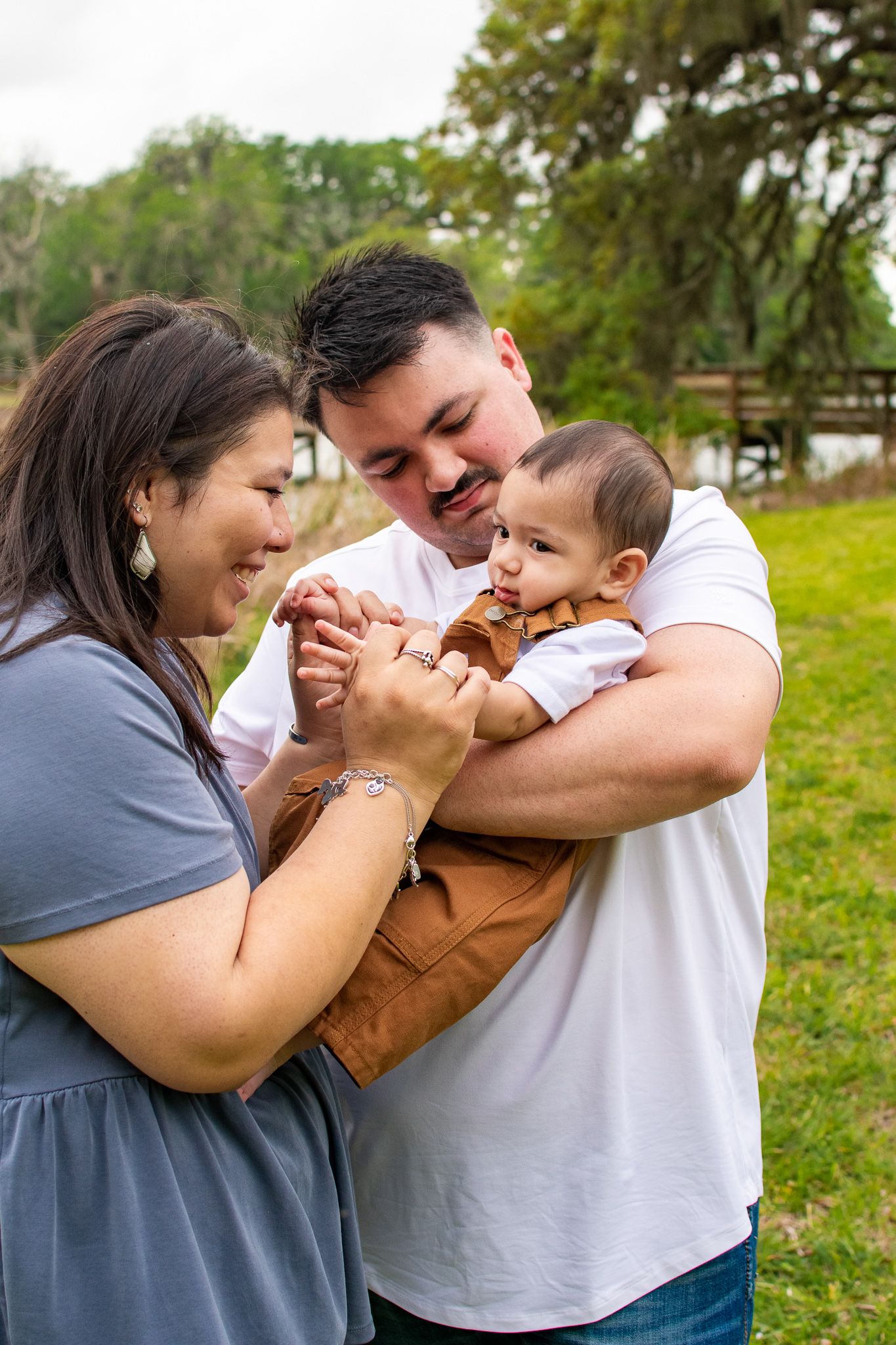 A loving family moment outdoors as parents play with their baby in a brown outfit on a sunny day.