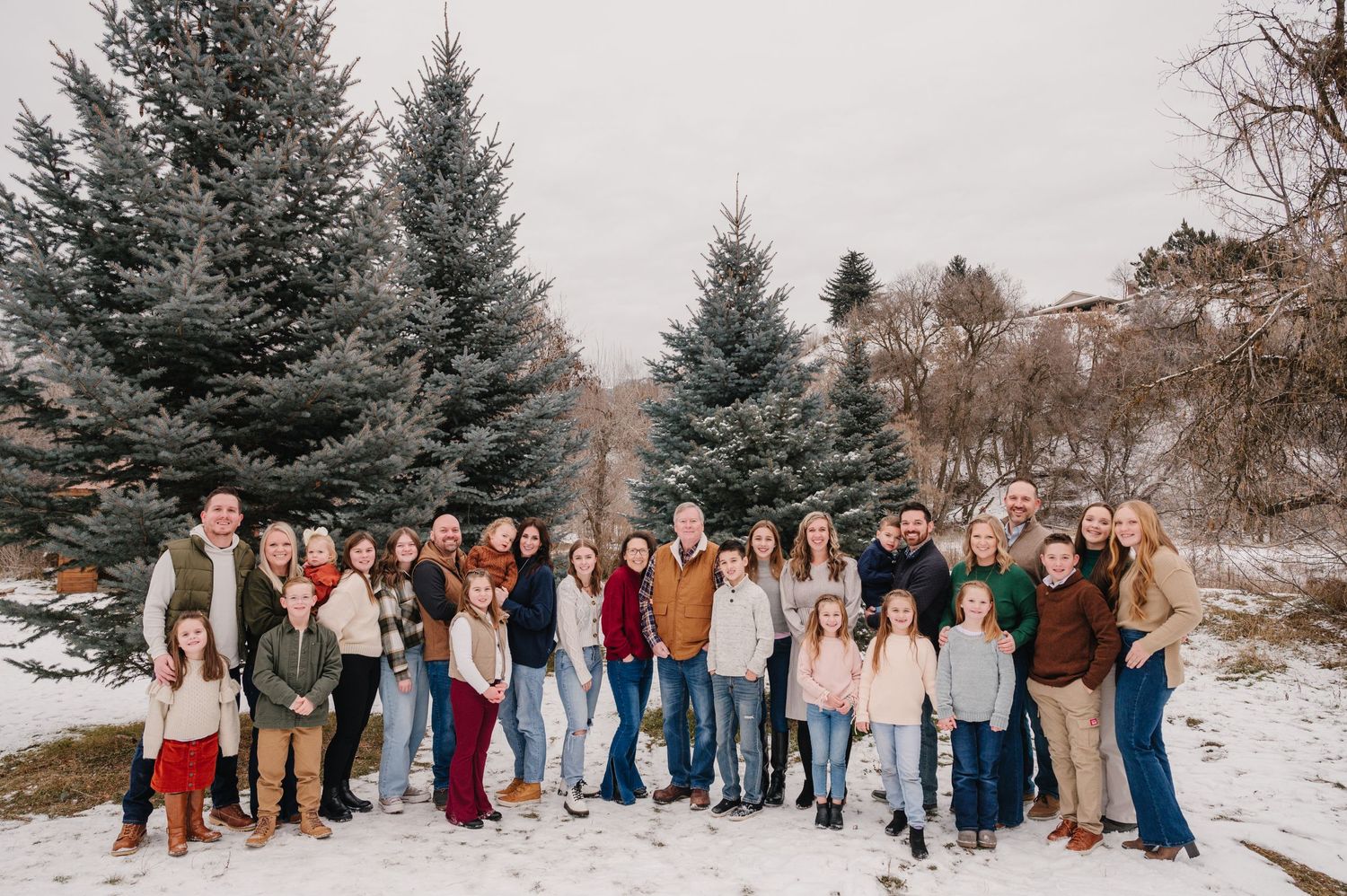 Large group photo of people gathered in front of snow-dusted evergreen trees during winter.