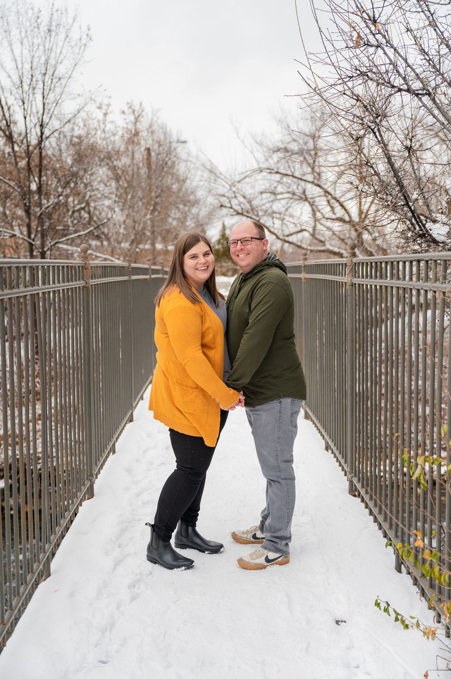 Couple standing close together on snow-covered bridge during winter.