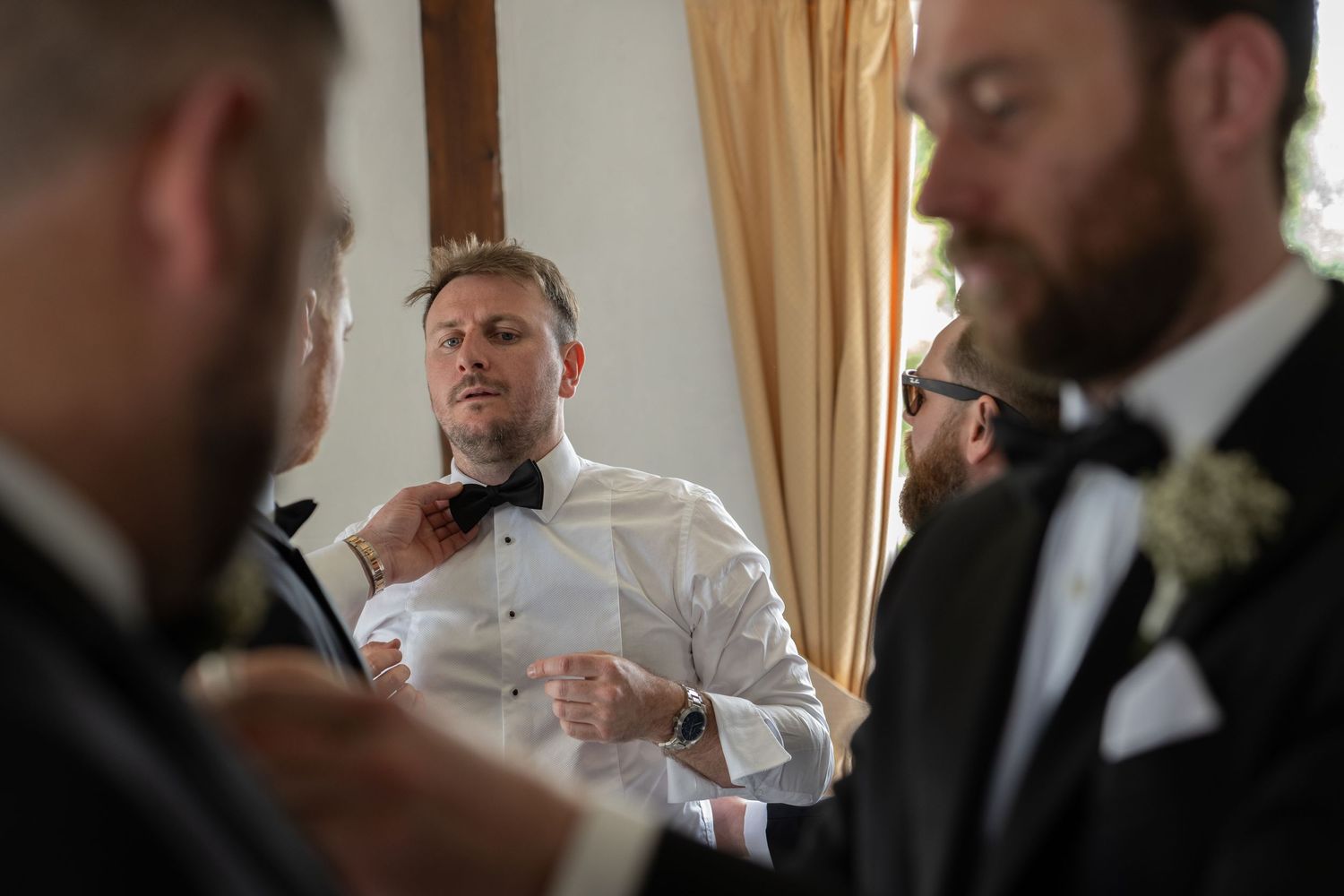 Groomsmen help adjust bow tie during wedding preparations.