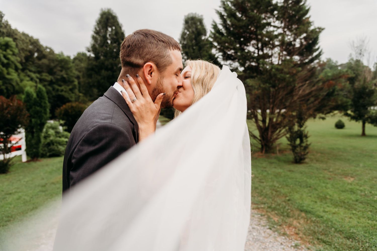 A romantic wedding moment captured as a couple kisses while the bride's veil flows in the wind.
