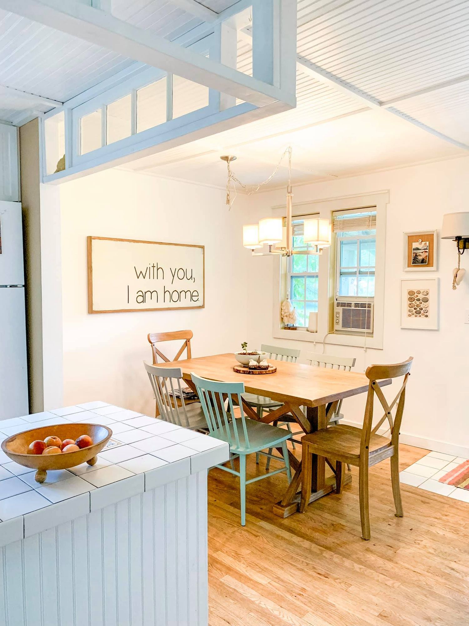 A bright coastal-style dining room with white walls, wooden floors, and a rustic dining table set under pendant lighting.