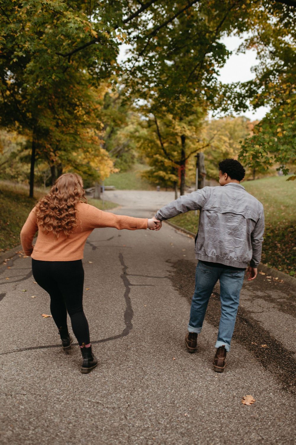 A couple holding hands while walking down a tree-lined autumn path.