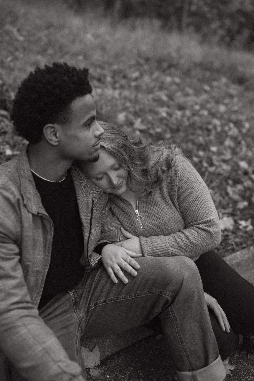 A romantic black and white portrait of a couple embracing on autumn ground.