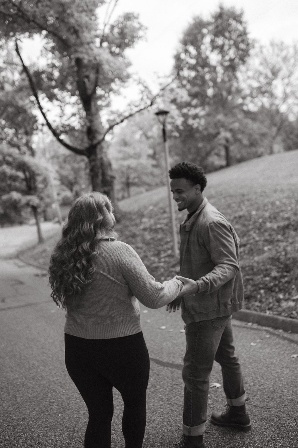A couple sharing a tender moment on a park path surrounded by fall trees.