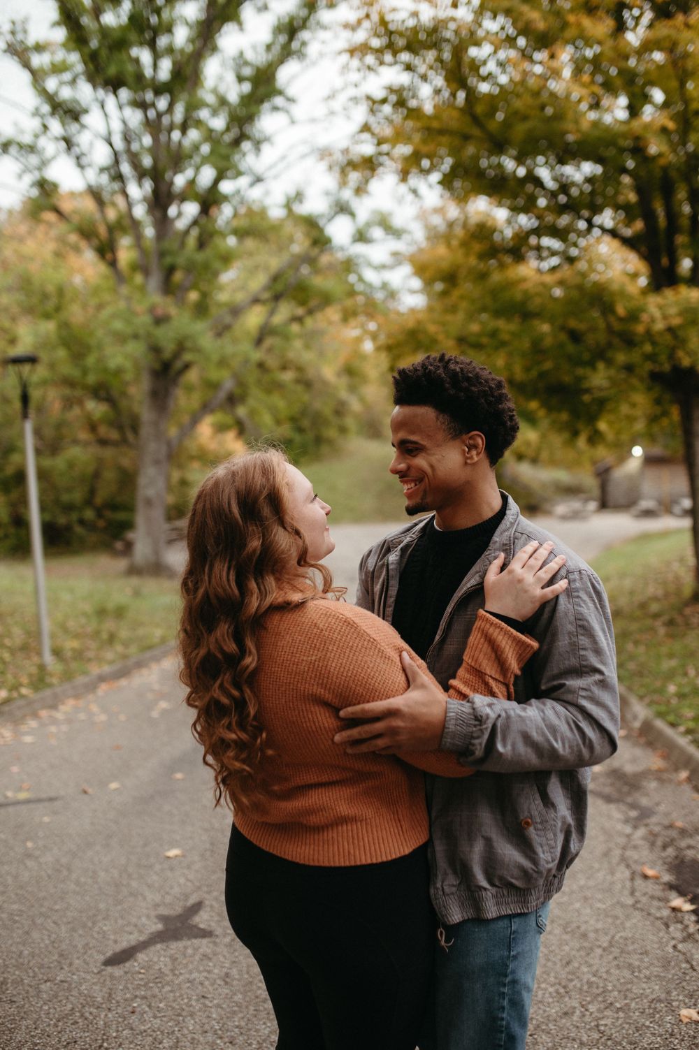 A couple embraces and shares a loving moment on a tree-lined pathway.