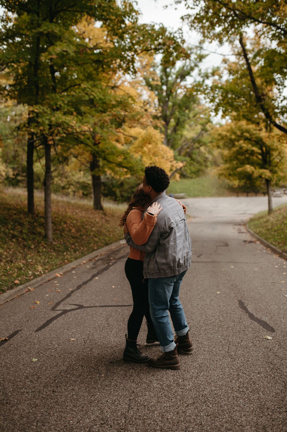 A couple embracing on a tree-lined path during autumn.