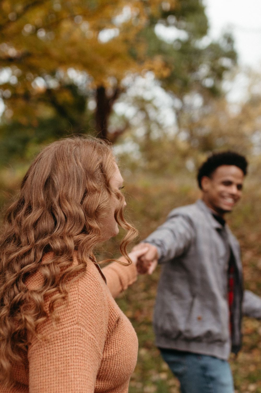 A couple laughs and dances together on a fall day in the park.